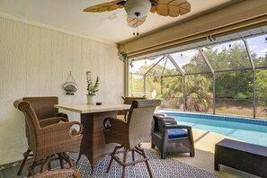 A room with wicker furniture, a table, and a view of a swimming pool.