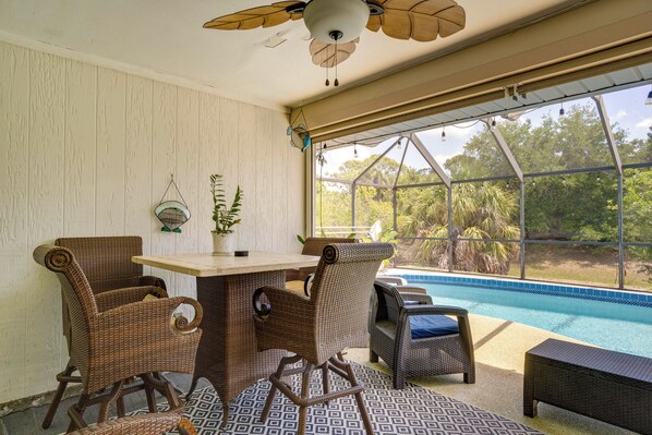 A room with wicker furniture, a table, and a view of a swimming pool.