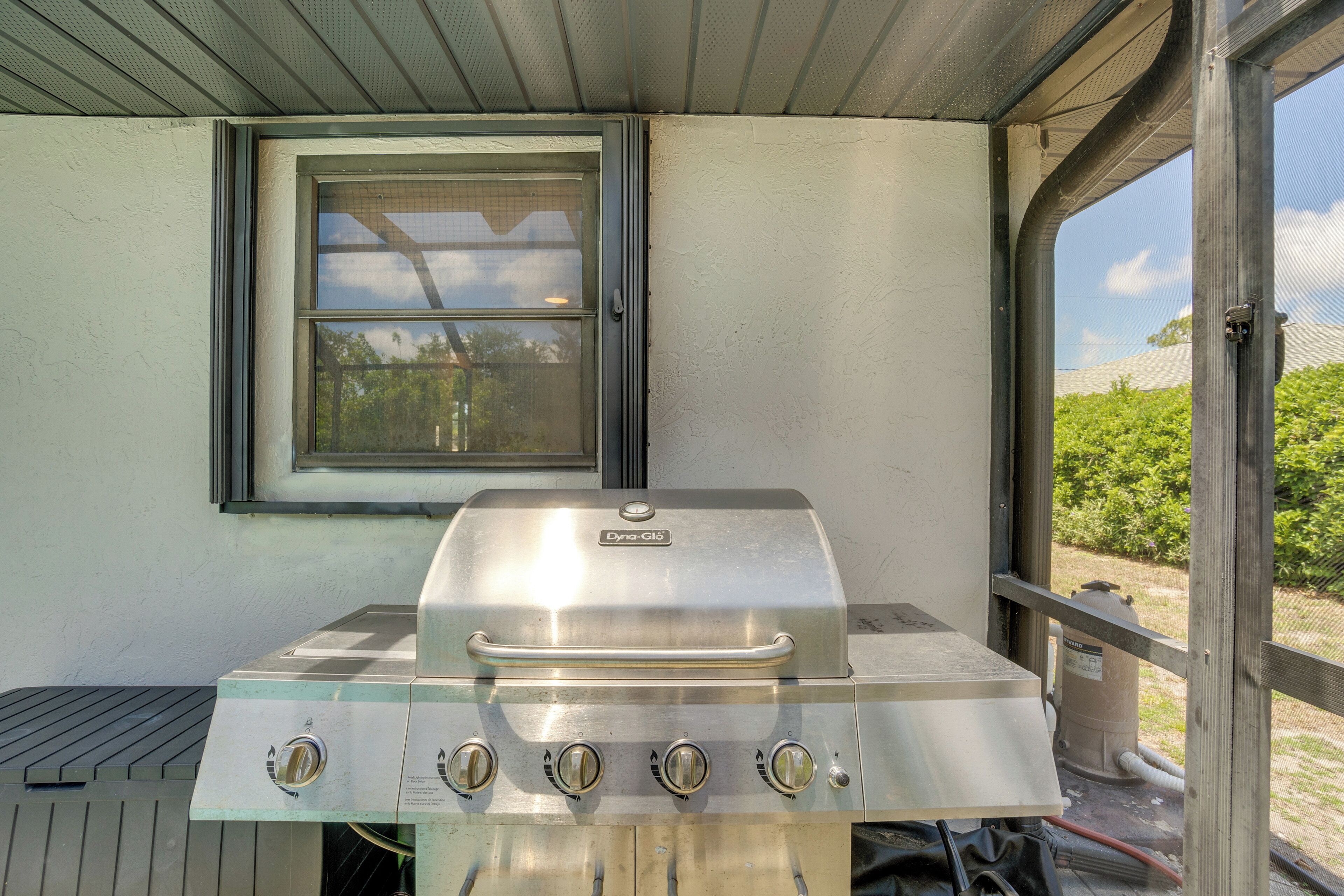 Un barbecue en acier inoxydable doté de quatre brûleurs, d’une fenêtre et offrant une vue sur la verdure environnante.