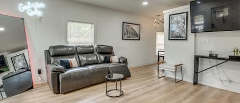 A modern living room with a leather sofa, a small round table, and a flat-screen TV mounted on the wall.