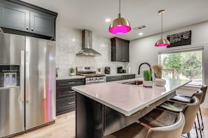 A modern kitchen with a stainless steel refrigerator, a central island with bar stools, a gas stove, and pendant lighting.