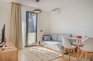 Ein modernes Wohnzimmer mit einer Couch, einem Esstisch, Stühlen, einem kleinen Teppich und einem Fenster mit Vorhängen.