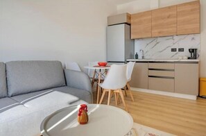 Ein modernes Wohnzimmer mit einem grauen Sofa, einem kleinen runden Tisch mit einer roten Flasche und einer Küchenzeile mit Holzschränken und einer Marmor-Spritzschutzwand.