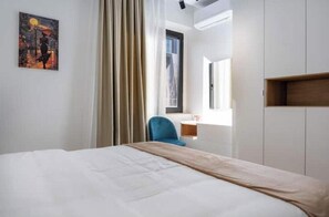 Ein Hotelzimmer mit einem Bett, einem Schreibtisch, einem Stuhl, einem Bild an der Wand und einem Fenster mit Vorhängen.