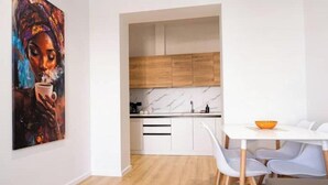 A modern kitchen with white cabinets, a marble backsplash, and a dining area with a white table and blue chairs. - Barrikada-E – Central Apartments with French Balcony & Netflix in Tirana (Tiranë)