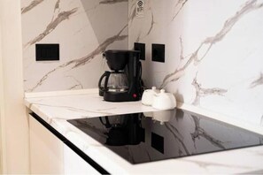 Eine Küche mit einer schwarzen Kaffeemaschine, einem weißen Wasserkocher und einer Marmor-Spritzschutzwand.