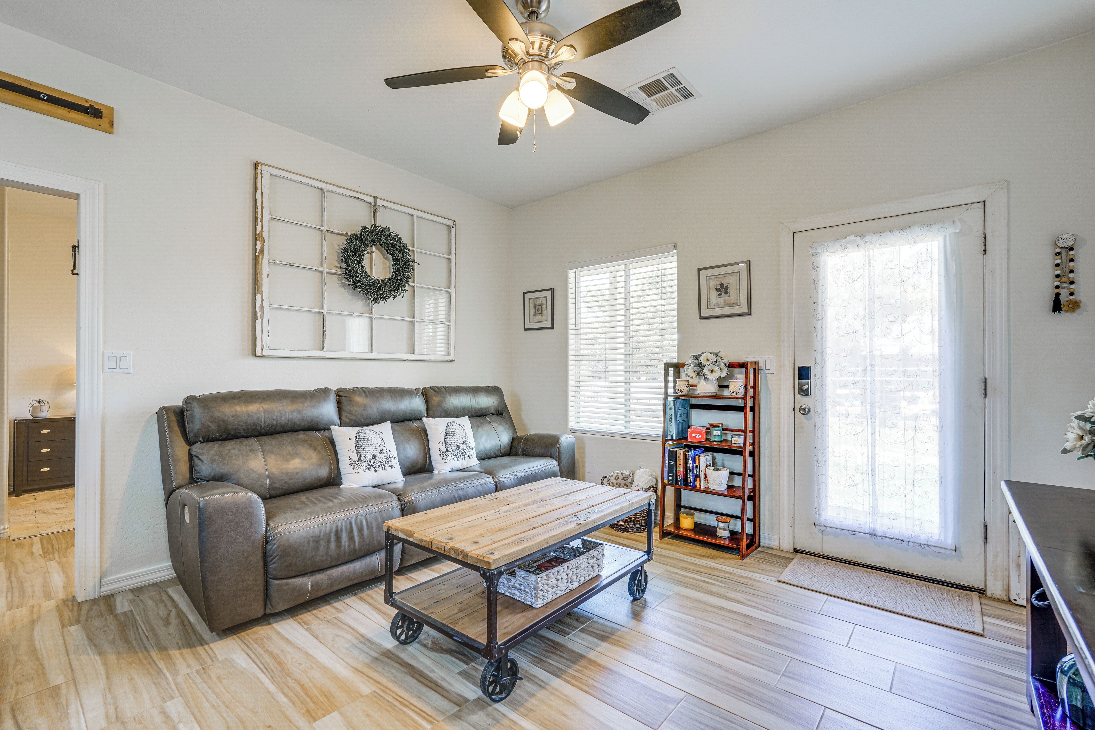 A living room with a leather sofa, a wooden coffee table with wheels, a ceiling fan, a bookshelf, and a door with a window.