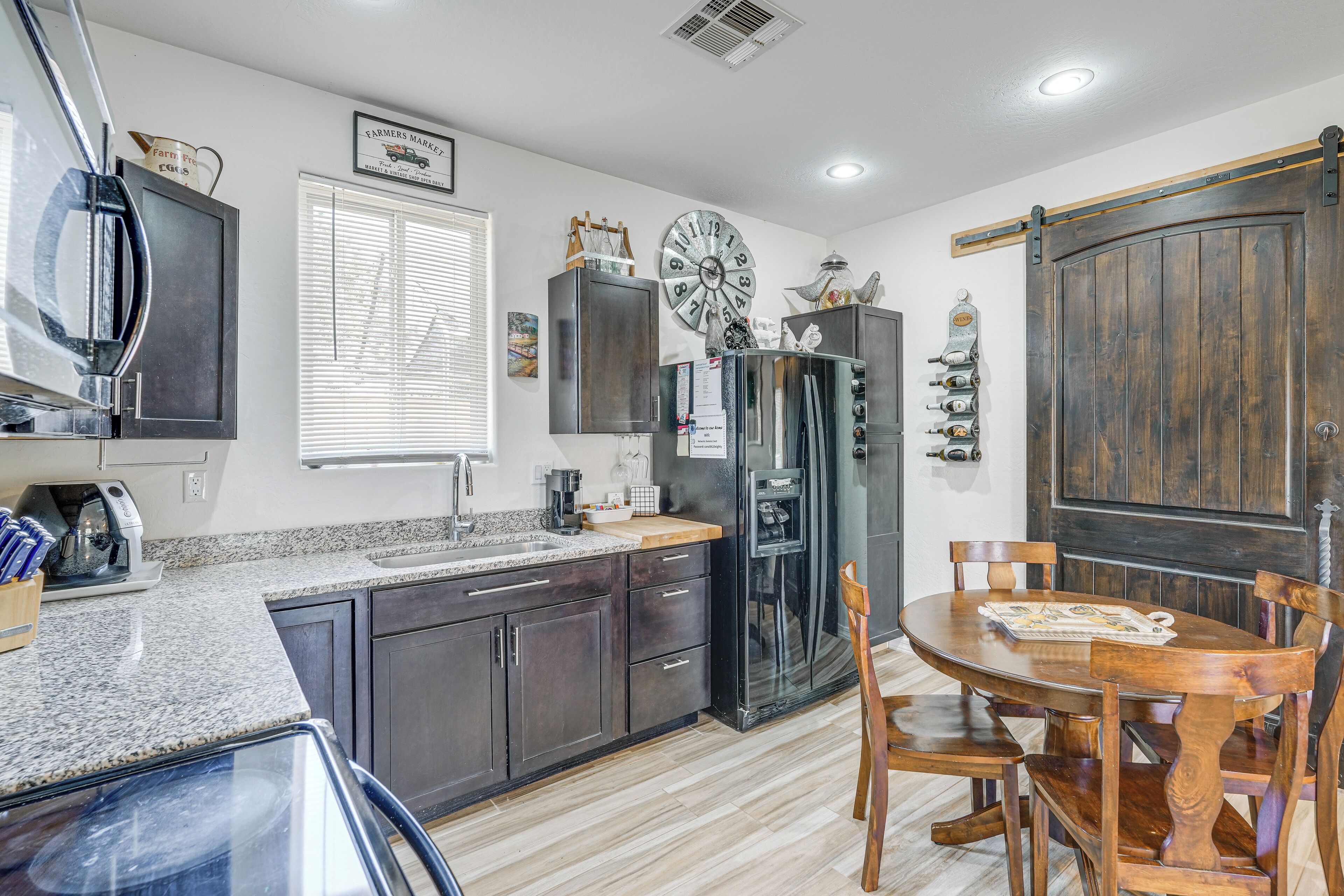 A kitchen with dark cabinets, a refrigerator, a clock, and a dining table with chairs.