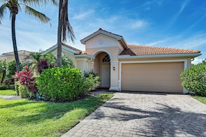 A residential house with a garage, a driveway, and well-maintained landscaping including palm trees and shrubs. - Extended Stay in Naples! Home w/ Community Perks (Naples)