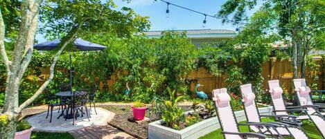 A patio with a table and chairs, a small garden with plants and a bird sculpture, and a row of sun loungers.