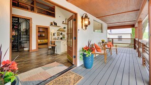 Um deck de madeira com área de estar externa, um vaso grande com planta e uma porta que dá para um espaço interior com cozinha e sala de jantar.