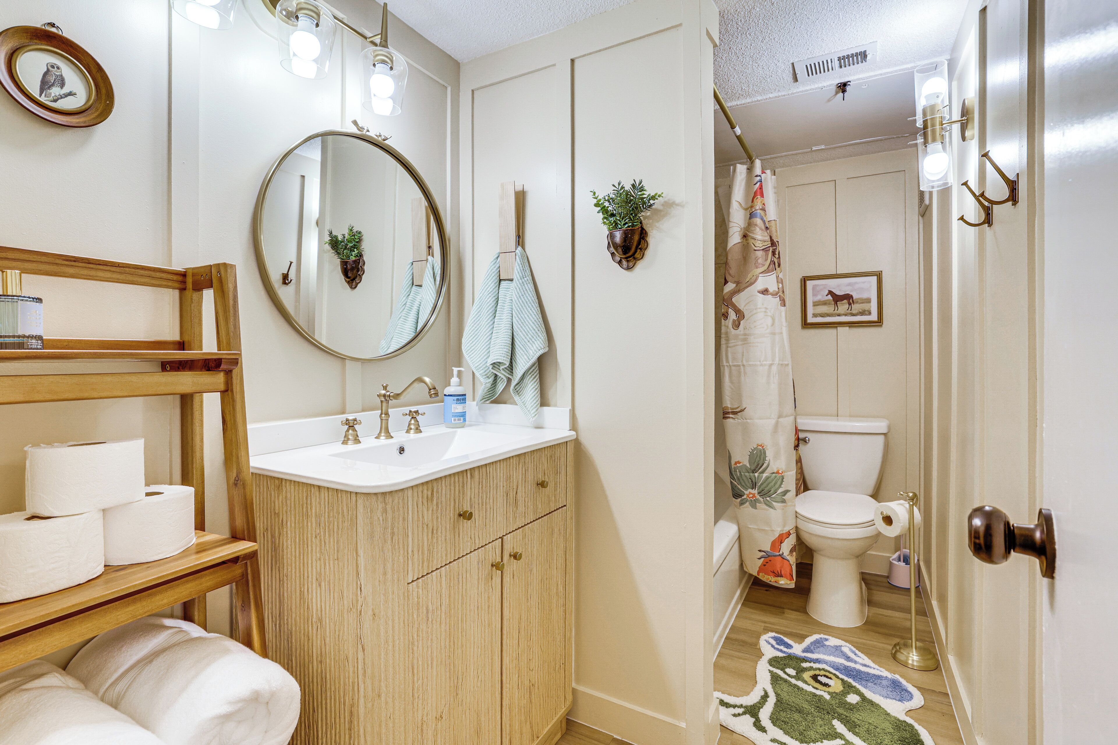 A bathroom with a wooden vanity, a round mirror, a toilet, and a shower curtain.