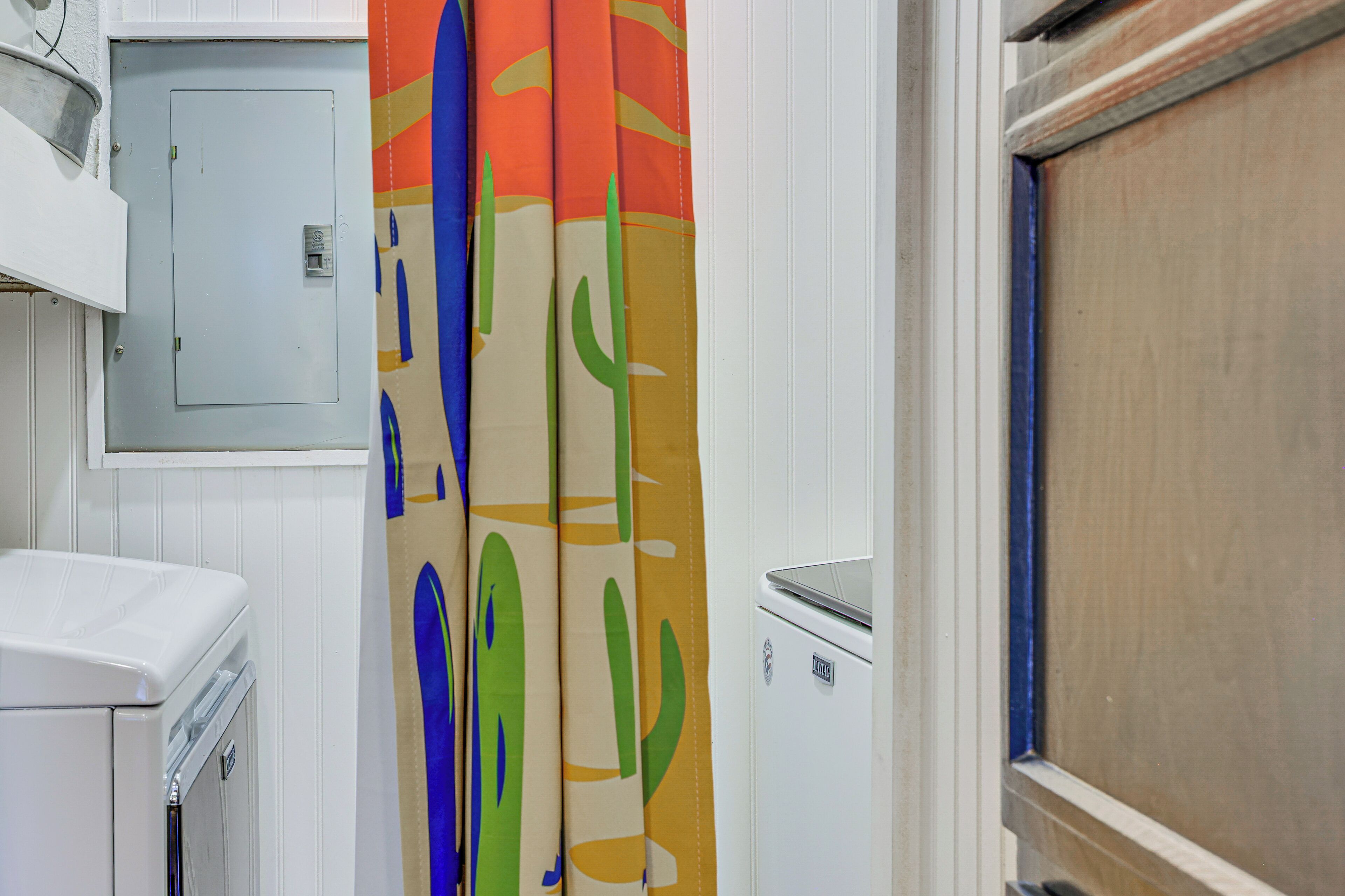 Un baño con una bañera blanca, una lavadora pequeña de color blanco y cortinas de ducha coloridas.