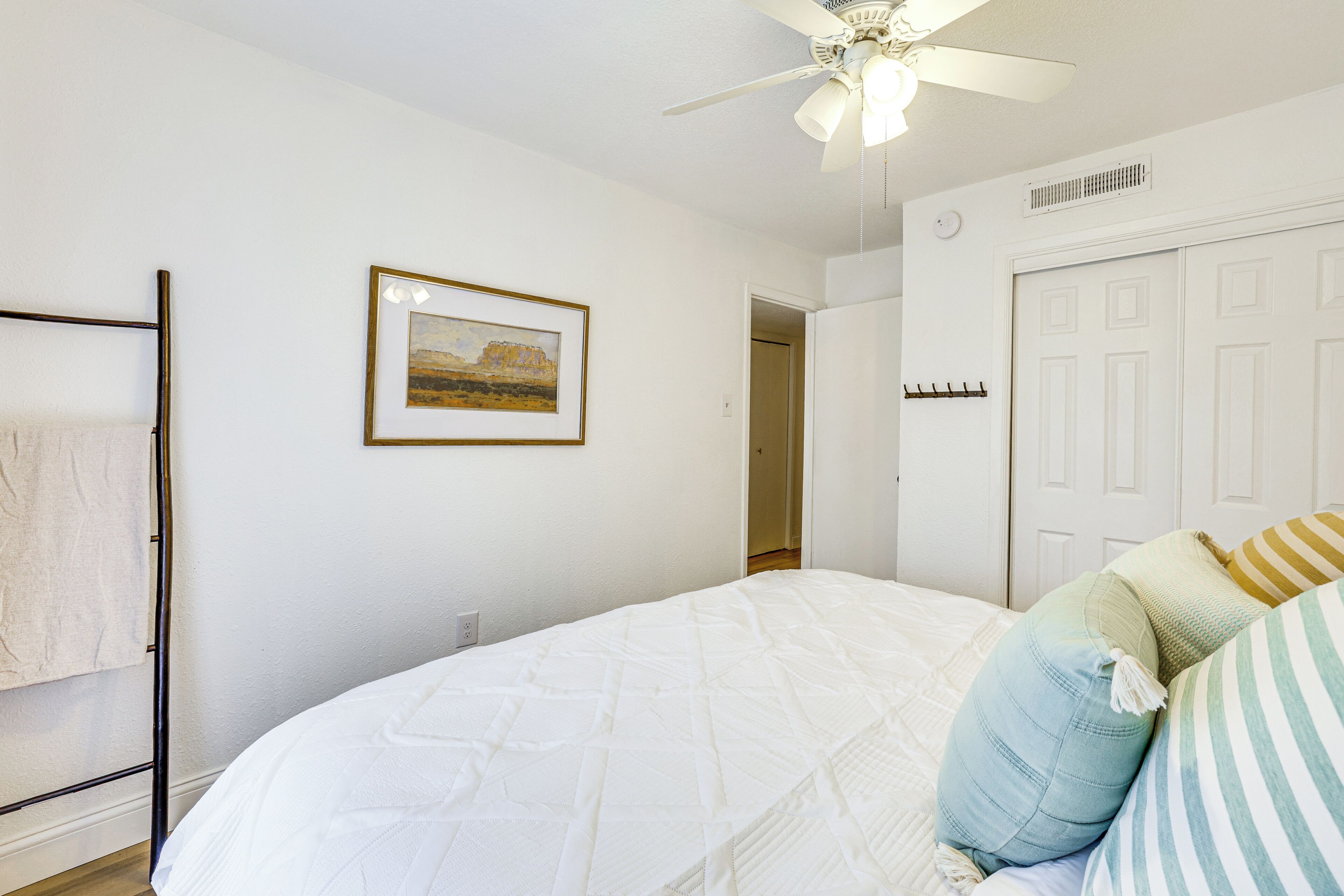 A bedroom with a bed, a ceiling fan, a door, and a framed picture on the wall.