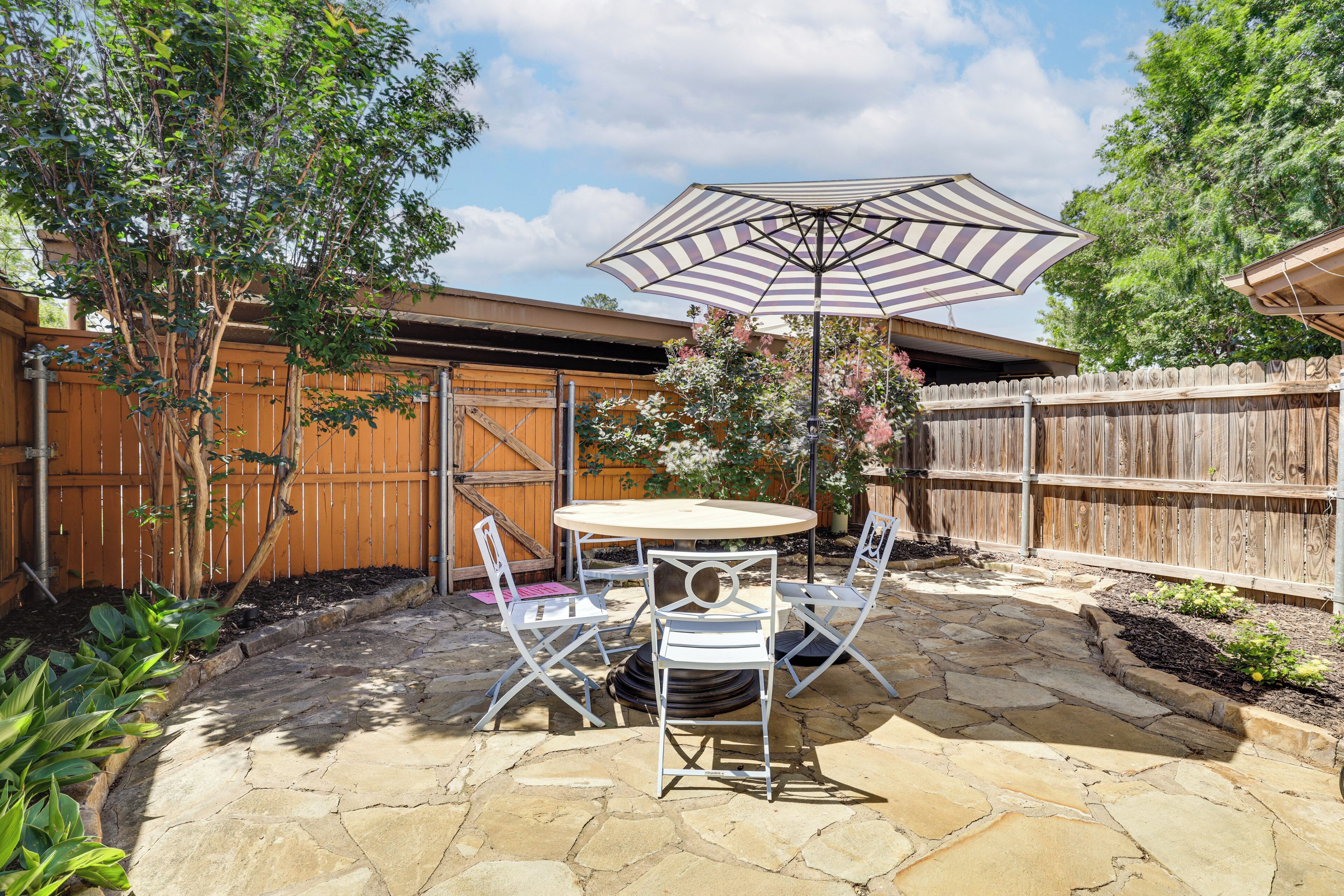 A patio with a round table and chairs, an umbrella, and a wooden fence.