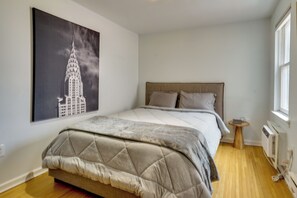 A bedroom with a bed, a small bedside table, a radiator, and a window. - Walkable Urban Retreat in Hoboken! (Hoboken)