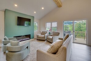 A spacious living area with a flat-screen TV, comfortable seating, a fireplace, and a view of the outdoors. - Margaritaville Access! Luxe Ozark Oasis w/ Hot Tub (Osage Beach)