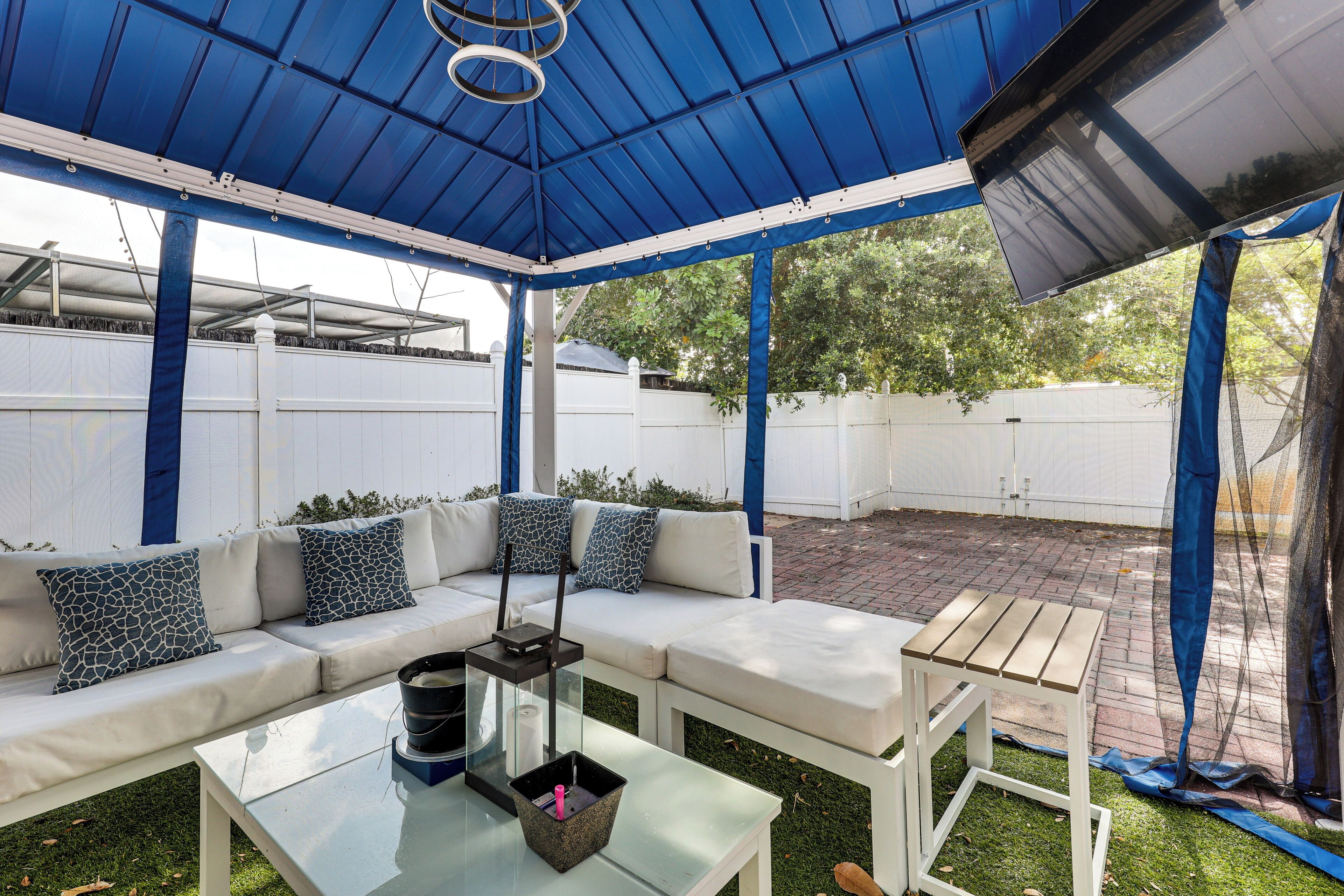 A covered patio with a white sofa, a glass table, and a metal chair.