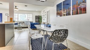 Un comedor moderno con una mesa de vidrio, sillas de metal y un cuadro de un paisaje urbano en la pared.