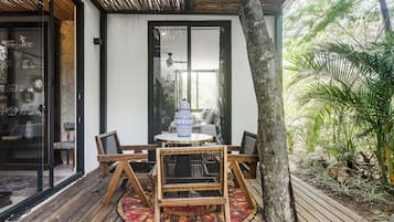 A wooden deck with a round table and chairs, a glass door, and a view of a garden.