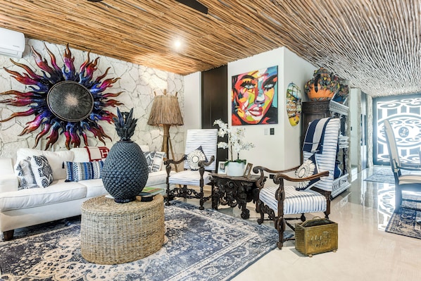 Un salon avec un canapé blanc, un tapis bleu à motifs, un élément décoratif mural en forme de soleil et un grand tableau abstrait.