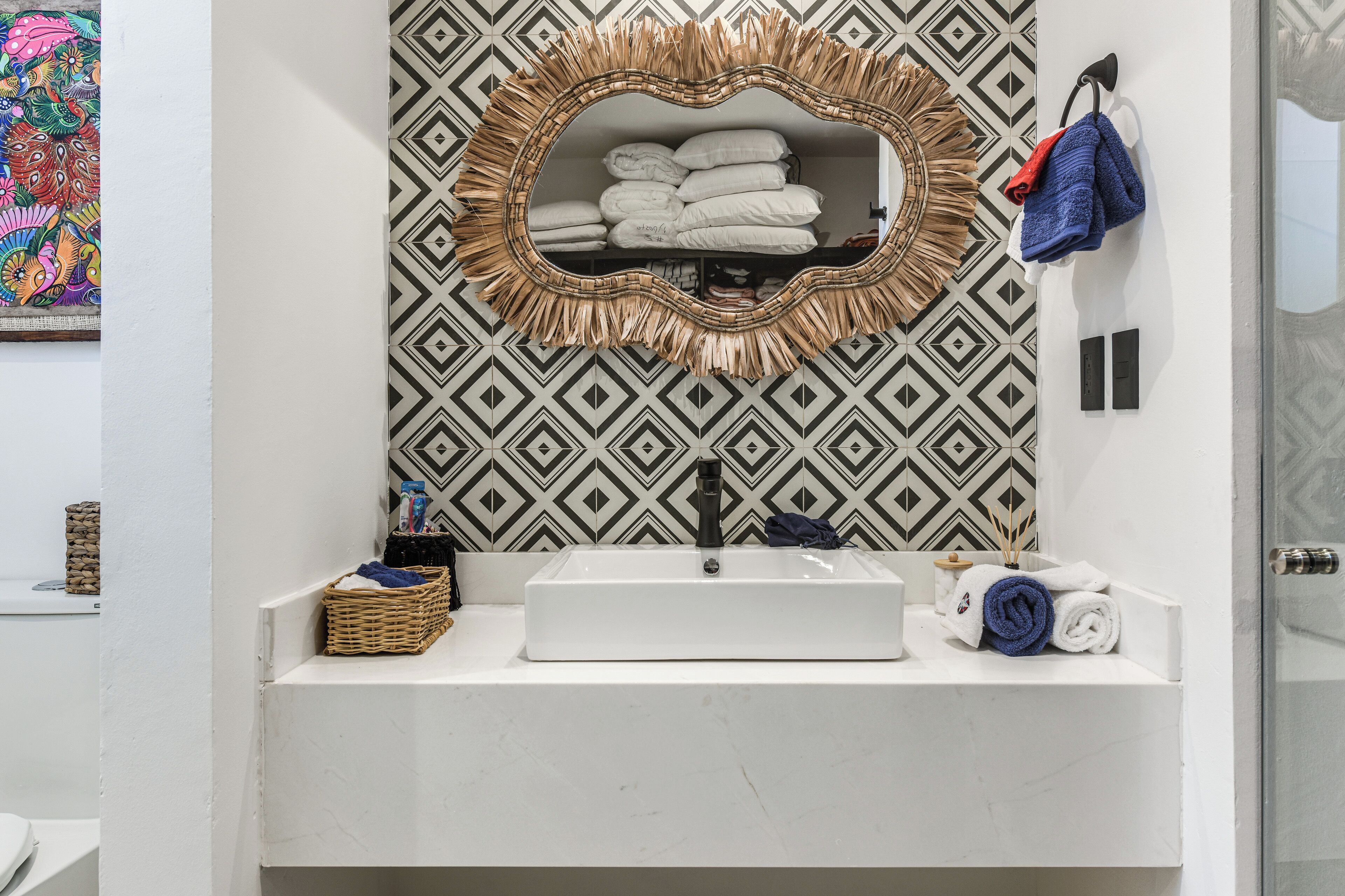 Un baño con lavamanos blanco, un espejo decorativo y pared con diseño.
