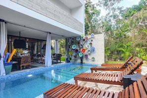 Un área de piscina moderna al aire libre con tumbonas de madera, un comedor y un muro decorativo.