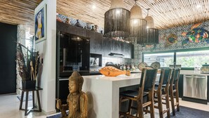 A modern kitchen with a central island, bar stools, a Buddha statue, and a decorative fish. - Private Xpu Ha Beach Access: 6,700-sq-ft Villa (Xpu-Ha)