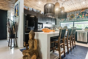 Une cuisine moderne dotée d’un îlot central, de tabourets de bar, d’une statue de Bouddha et d’un poisson décoratif.