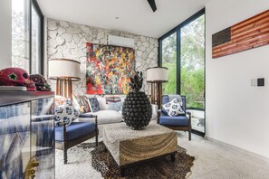 A modern living room with a stone wall, a colorful abstract painting, and a large window.