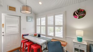 Ein Zimmer mit weißer Tür, einem Fenster mit Rollo, einem Tisch mit Lampe und einem Stuhl.