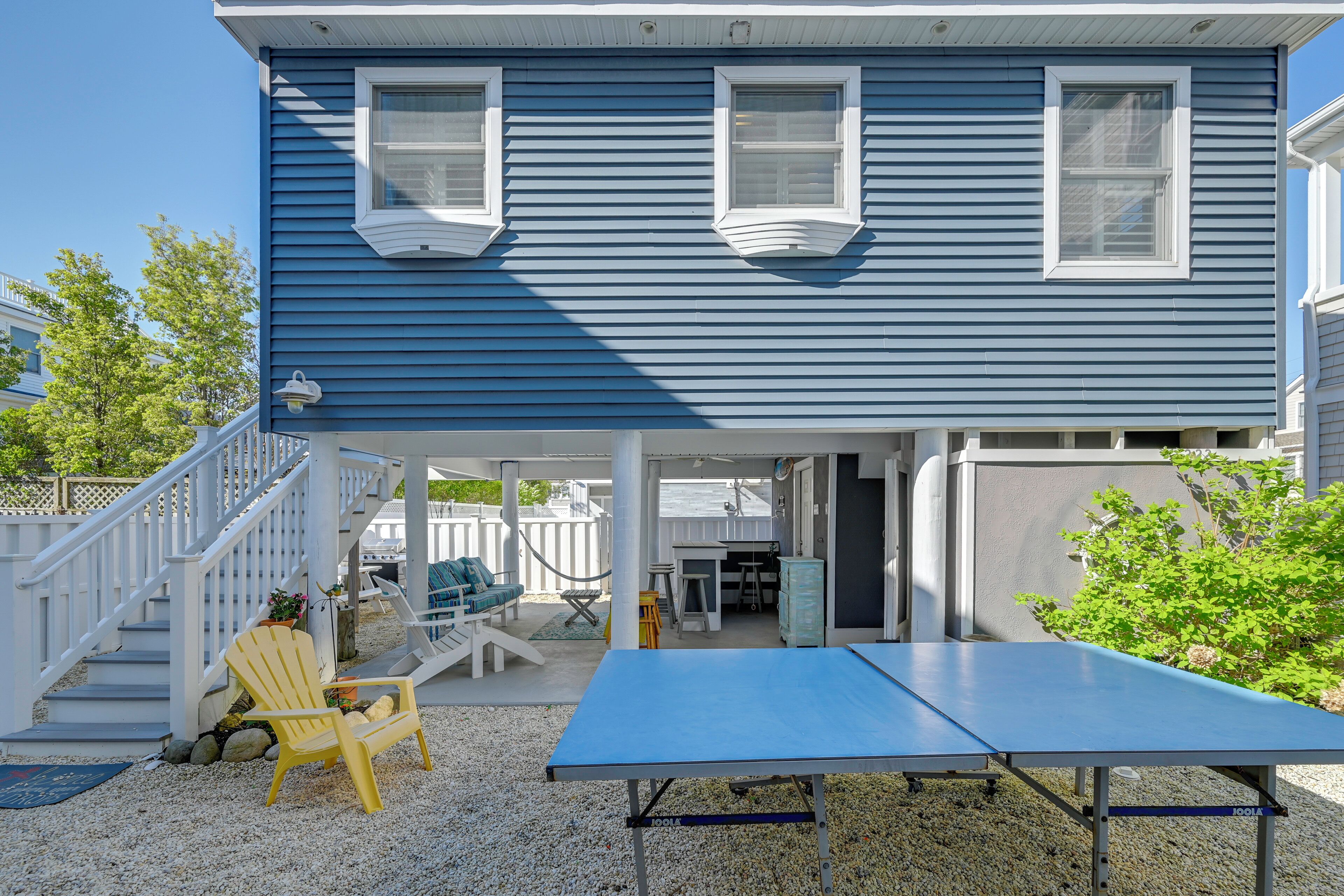 A blue house with a covered porch, a ping pong table, and a yellow Adirondack chair.