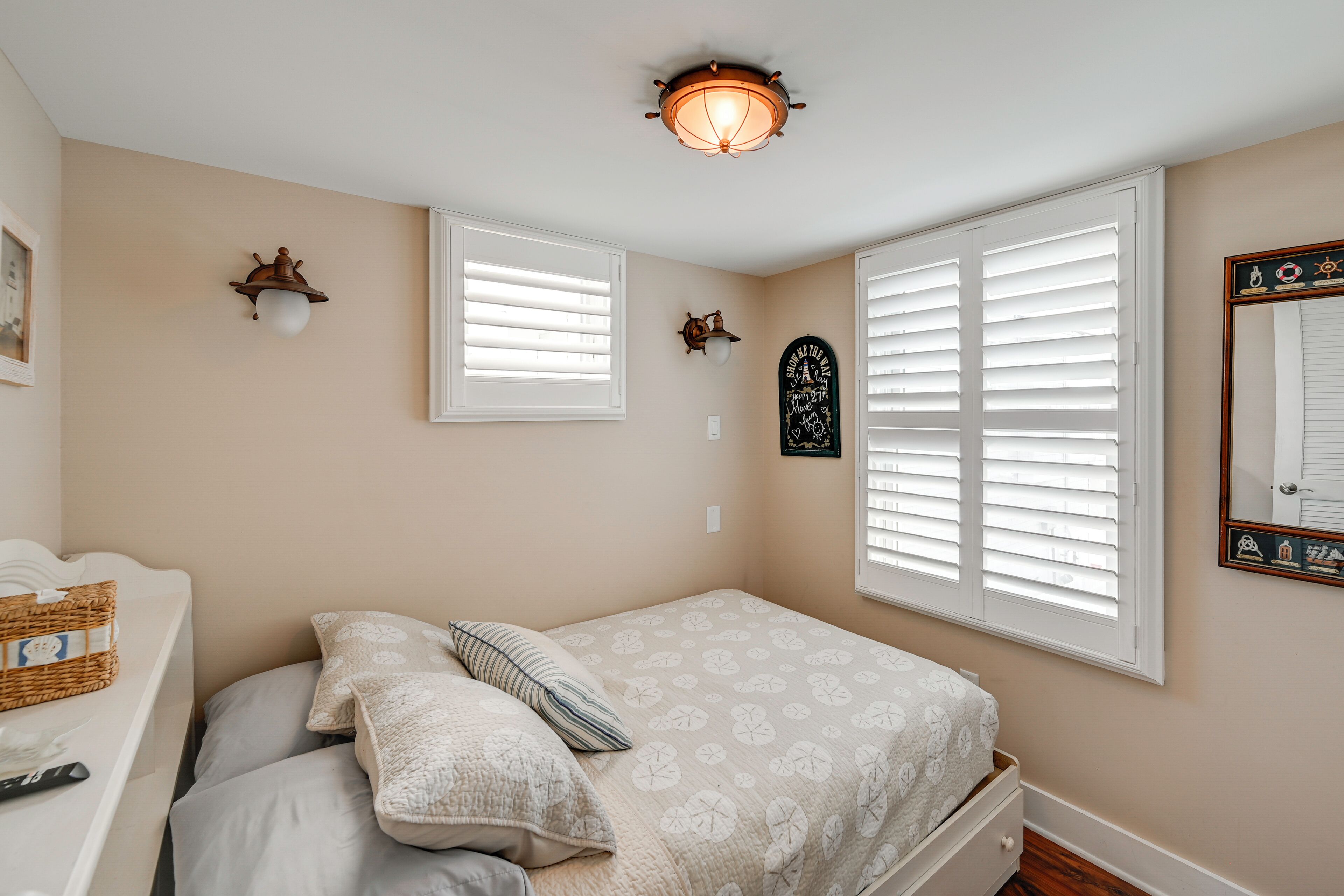 A bedroom with a bed, two wall-mounted light fixtures, a window with blinds, and a wall-mounted mirror.