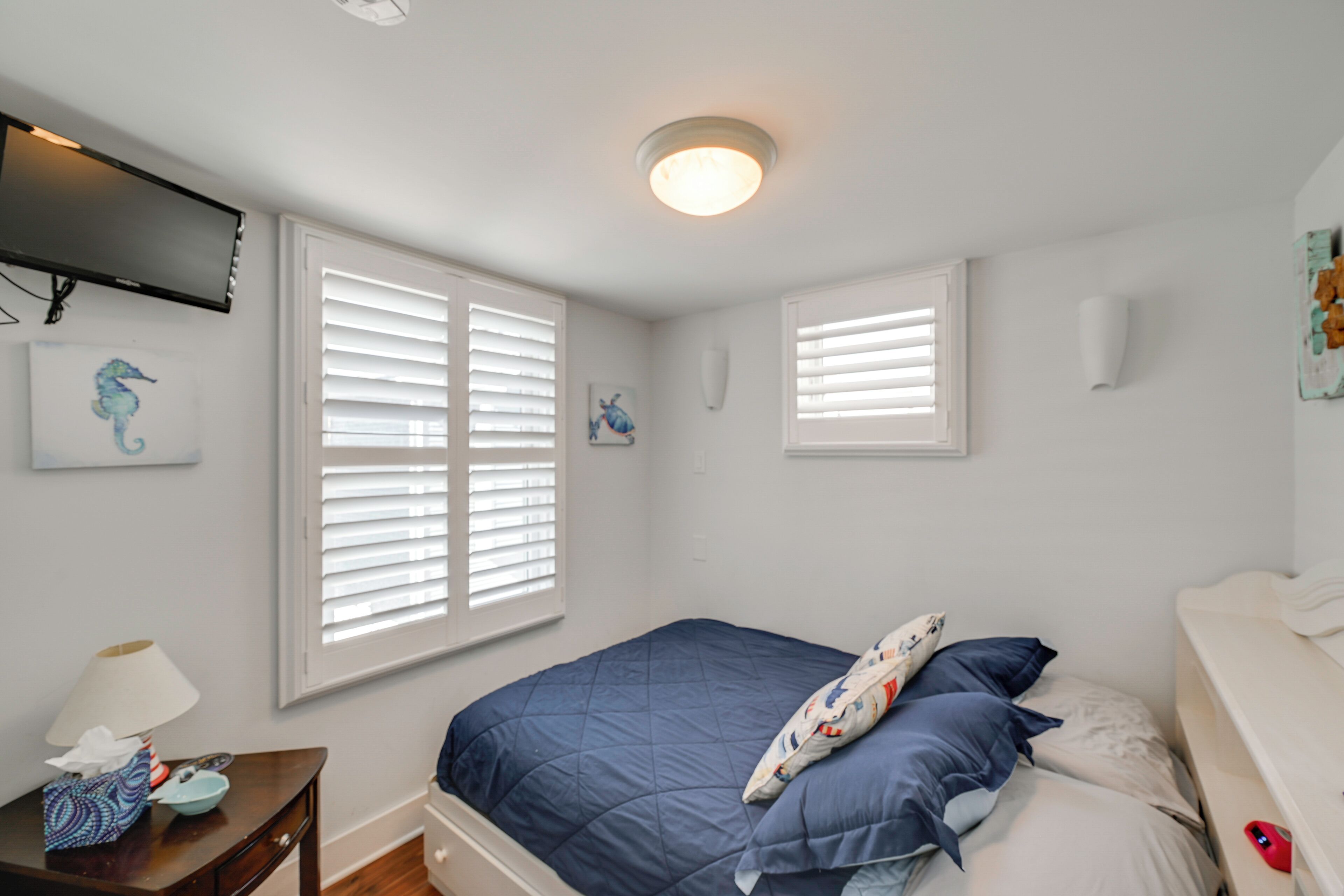 A bedroom with a bed, a TV mounted on the wall, and a window with blinds.