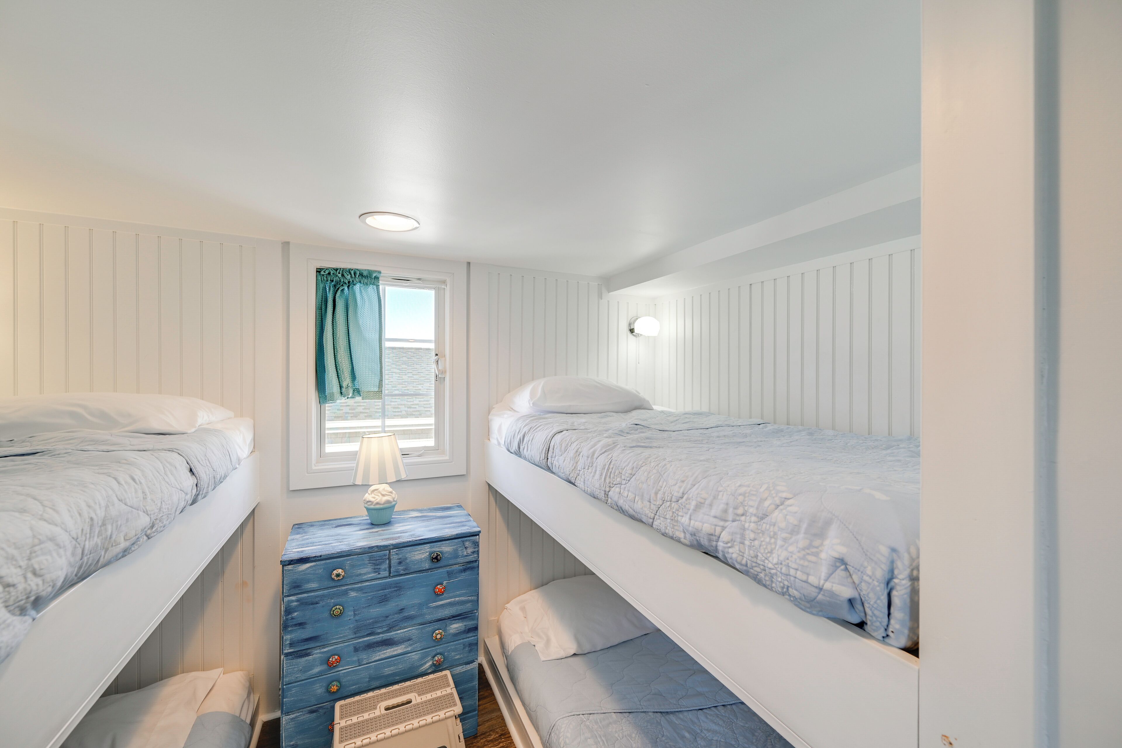 Une chambre avec deux lits superposés, une fenêtre avec des rideaux, une commode et une lampe.
