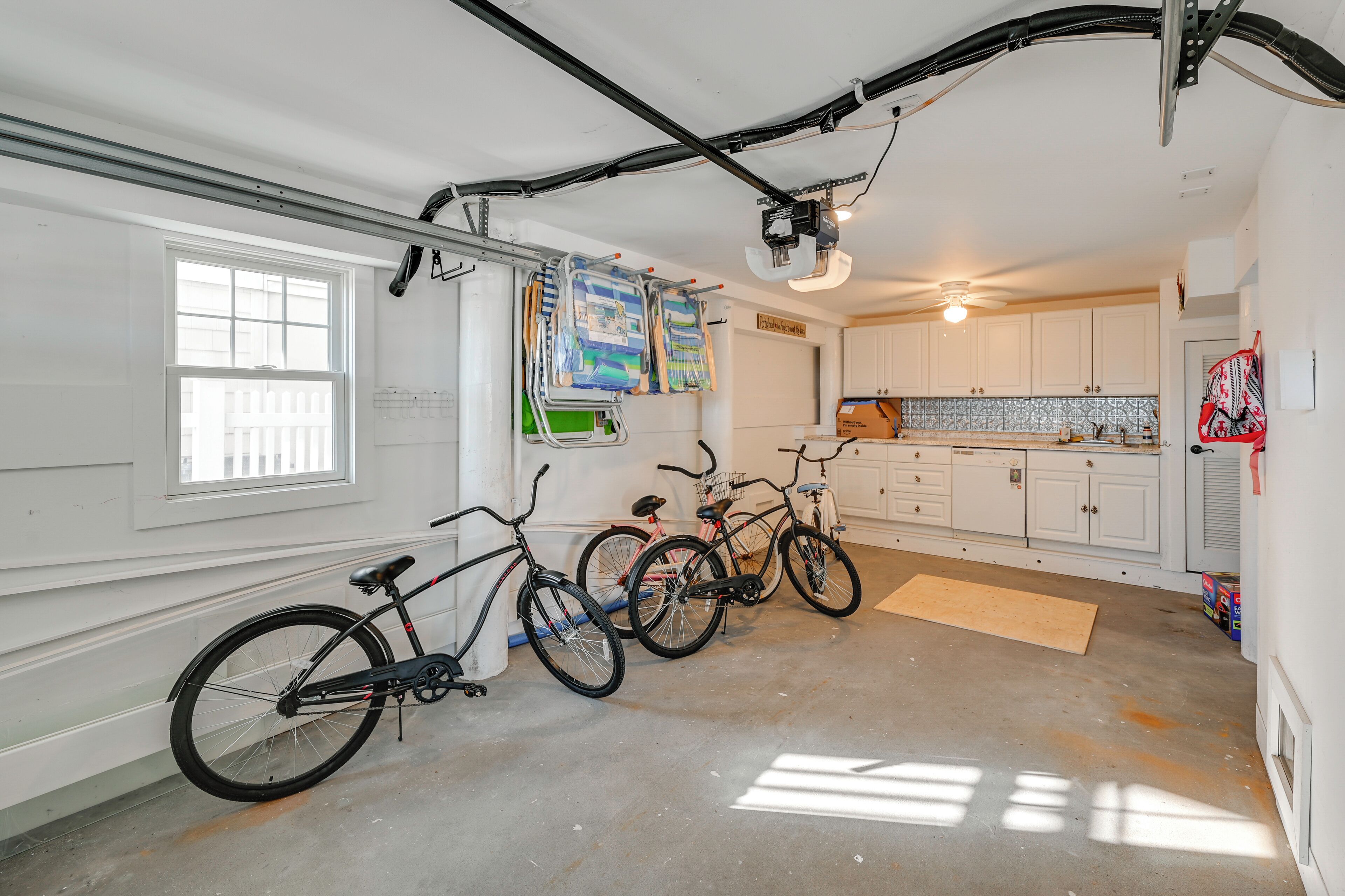 A garage with bicycles, a ceiling fan, and a kitchen area with cabinets and a countertop.