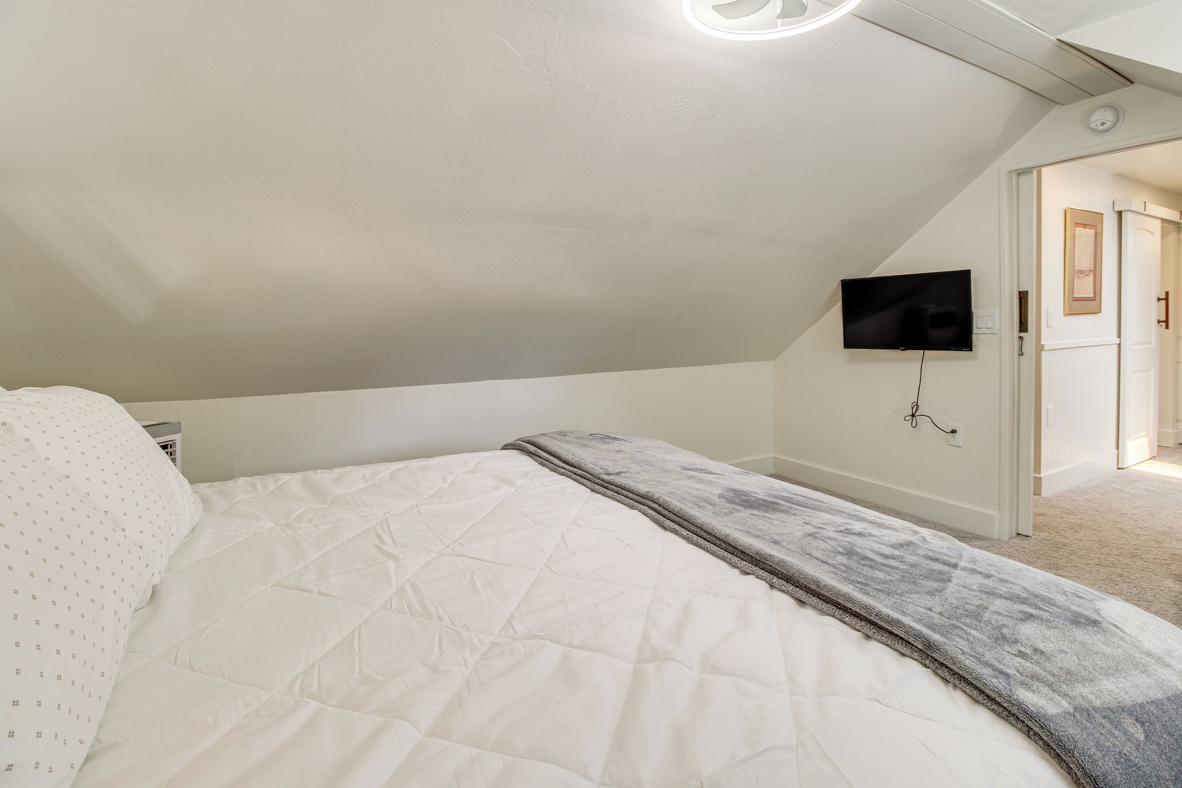 Un dormitorio con cama, televisor montado en la pared y una puerta que da a otra habitación.