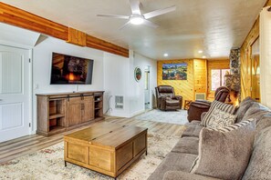 A living room with a wooden ceiling, a ceiling fan, a large flat-screen TV, a leather armchair, a sofa, and a coffee table. - Game Room + Fireplace! Family Retreat in Pinetop (Pinetop)