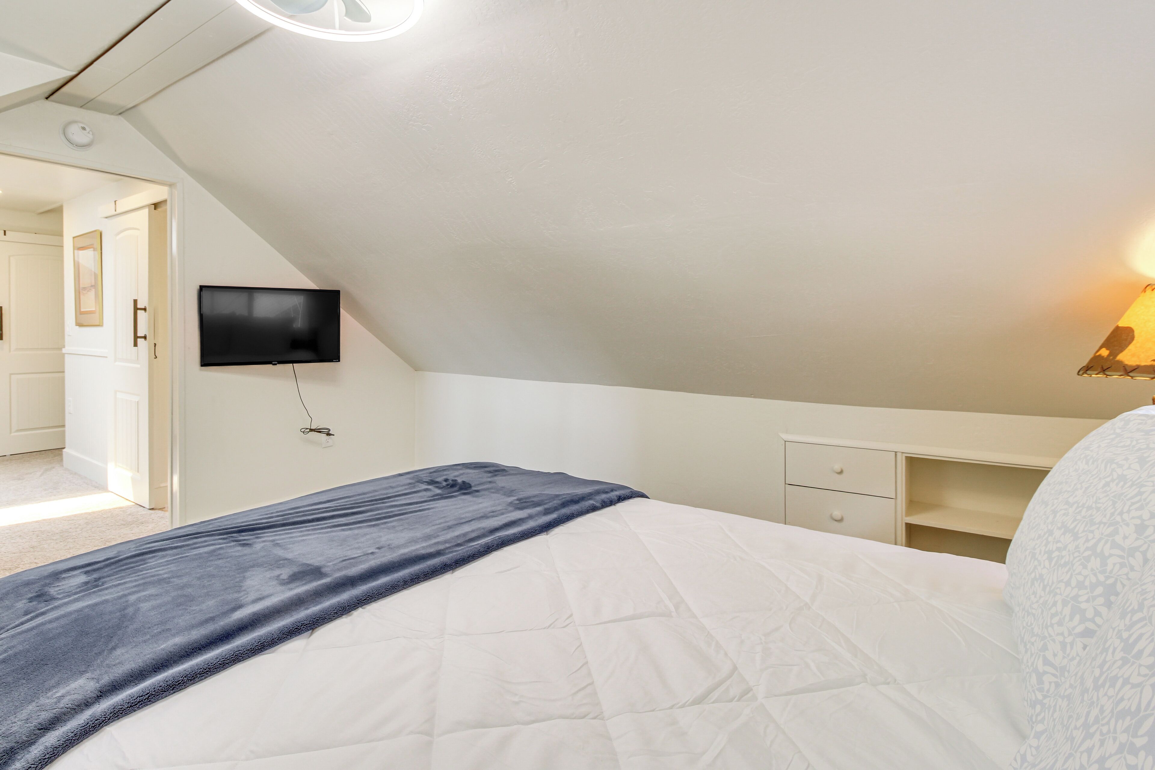 Een slaapkamer met een bed, een tv aan de wand, een nachtkastje en een lamp.
