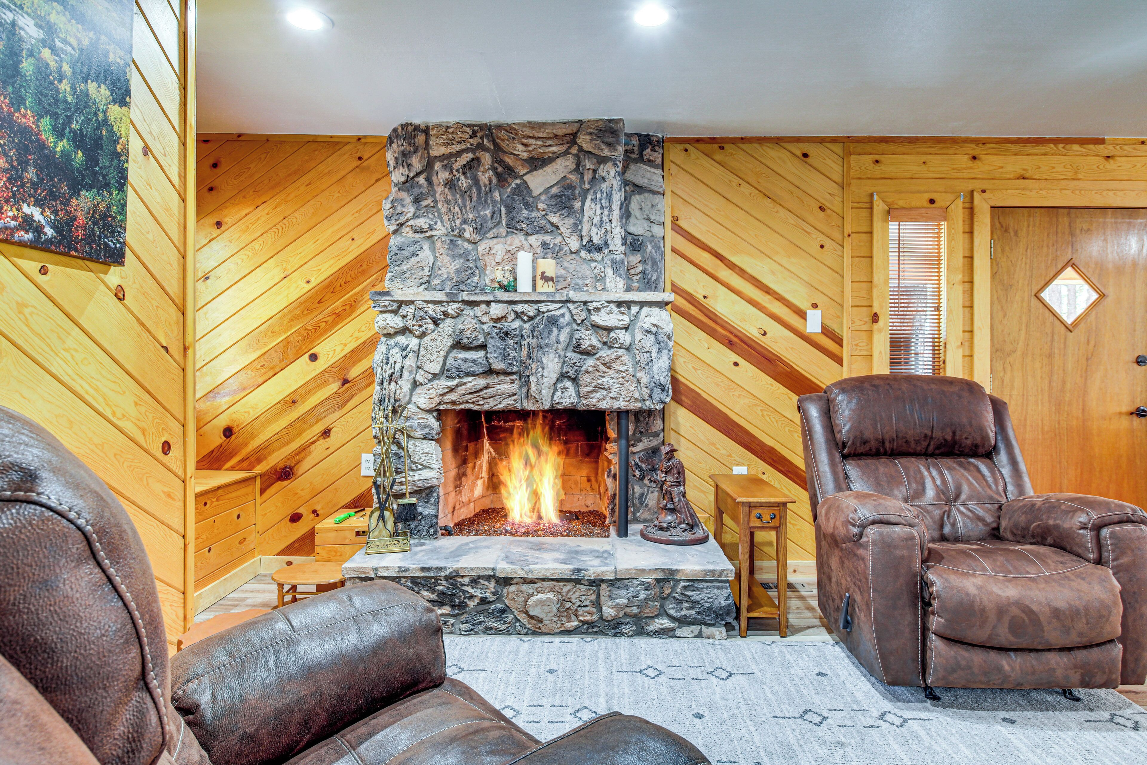 A cozy living room with a stone fireplace, leather recliner, and wooden walls.