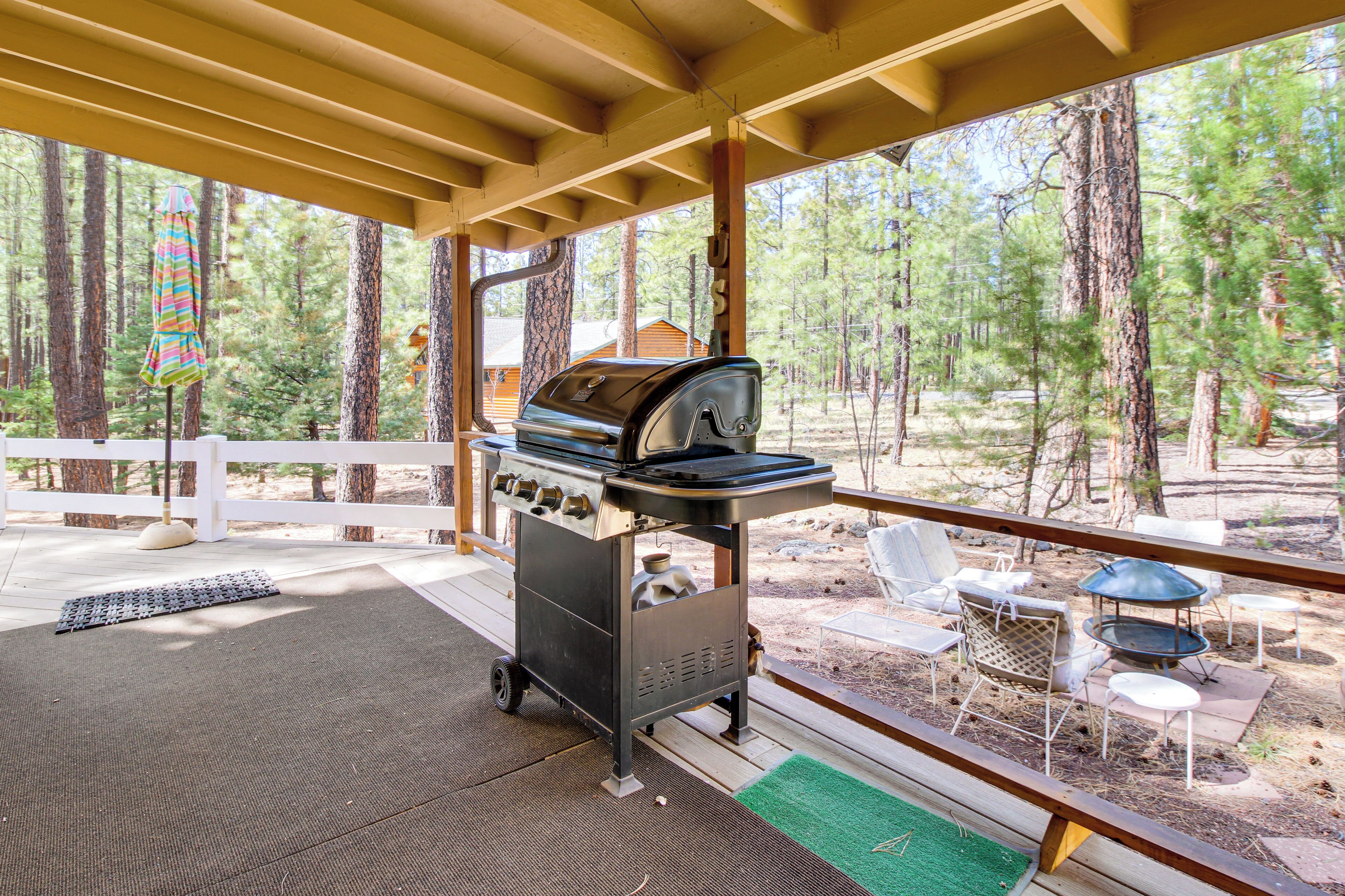 A covered outdoor area with a grill, seating, and a view of a forest.