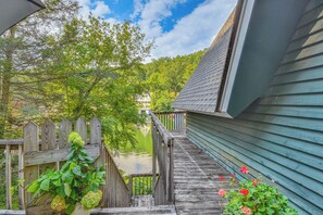 A wooden deck leading to a house with a green siding exterior, a wooden fence, and a body of water in the background. - Waterfront Lake Lure A-frame w/ Dock & Scenic Deck (Lake Lure)
