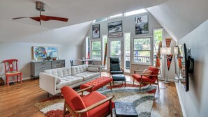 A spacious living room with a ceiling fan, a white sofa, red and black chairs, a gray cabinet, and artwork on the walls. - Waterfront Lake Lure A-frame w/ Dock & Scenic Deck (Lake Lure)