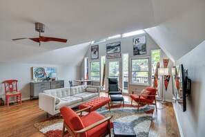 A spacious living room with a ceiling fan, a white sofa, red and black chairs, a gray cabinet, and artwork on the walls. - Waterfront Lake Lure A-frame w/ Dock & Scenic Deck (Lake Lure)