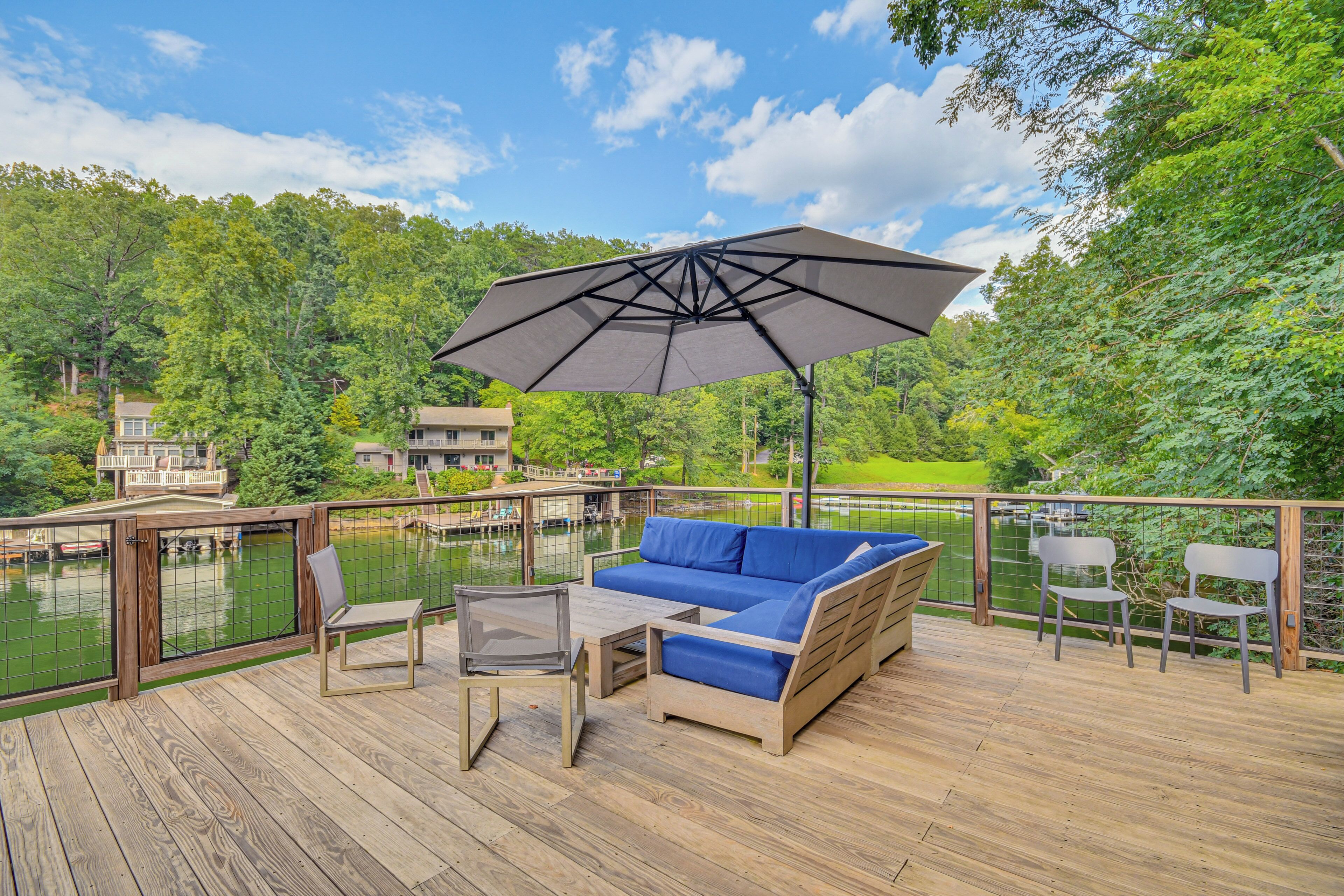 A wooden deck with a blue sofa, a table, and chairs, overlooking a body of water and greenery.