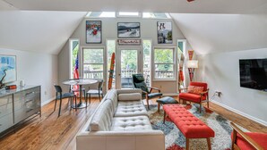 A spacious loft with a dining area, a large sofa, and a TV. - Waterfront Lake Lure A-frame w/ Dock & Scenic Deck (Lake Lure)