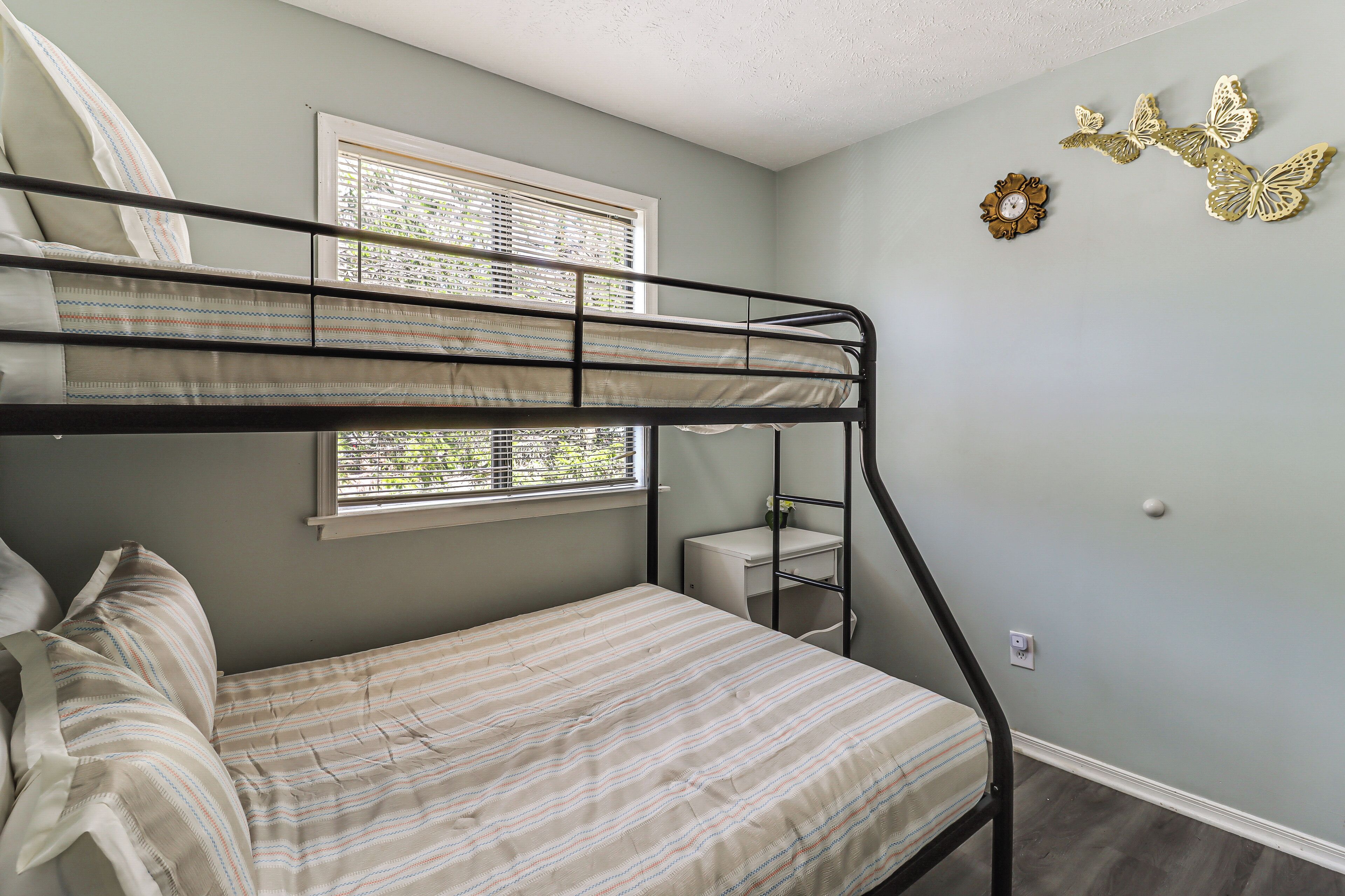 A bunk bed room with a window, a desk, and decorative butterfly wall art.