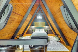 Un dormitorio acogedor en el ático, con techo inclinado, cama, mesitas de noche y una lámpara colgante.