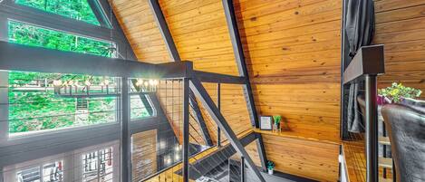 A wooden interior with a staircase, large windows, and a view of greenery outside.