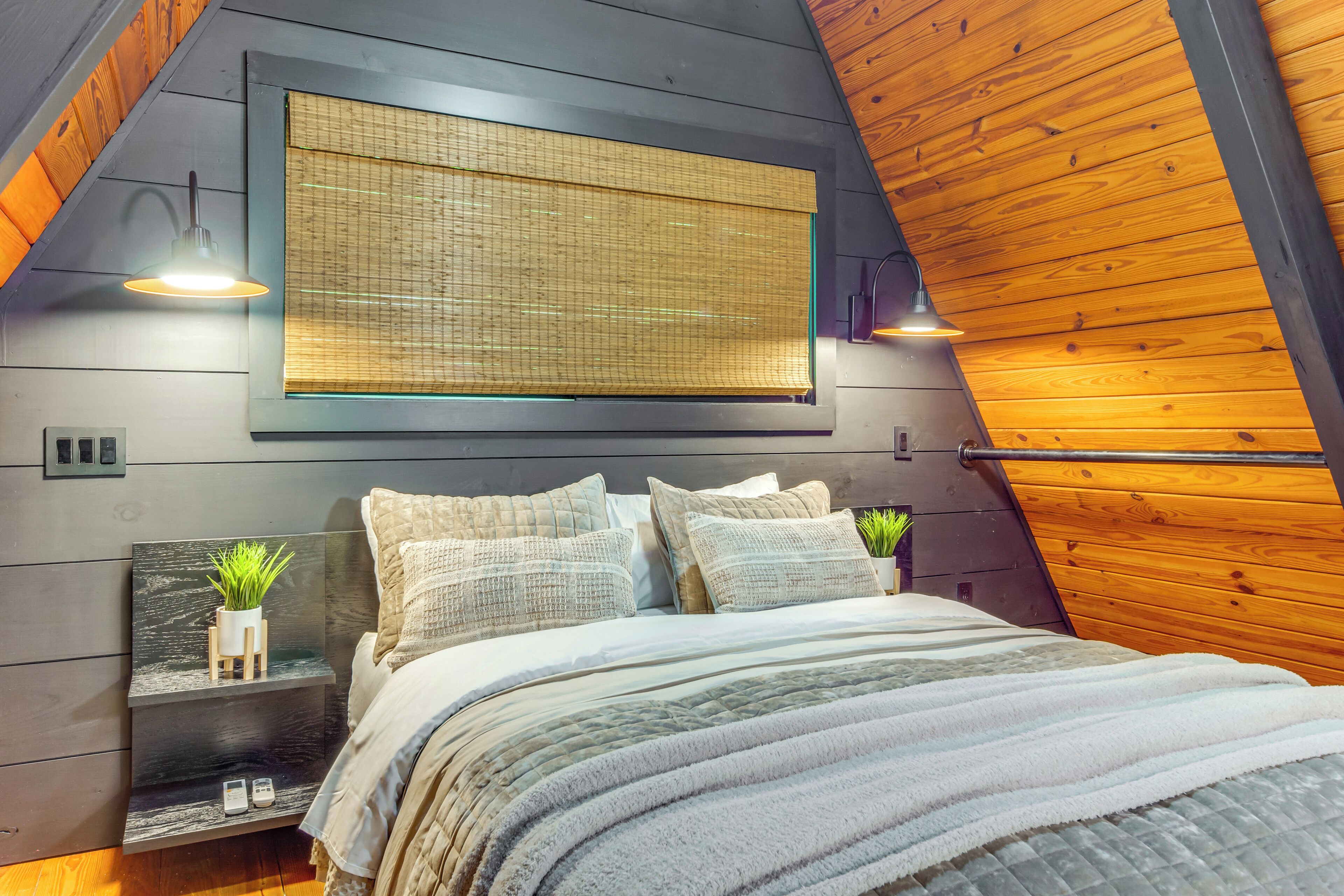 A bedroom with a bed, bedside tables, a hanging light, and a window with a view.